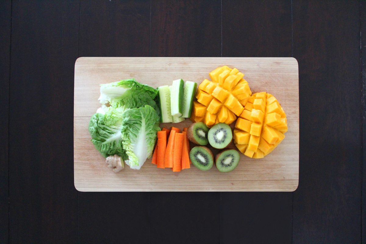 Sliced fruits and vegetables placed on a wooden chopping board.