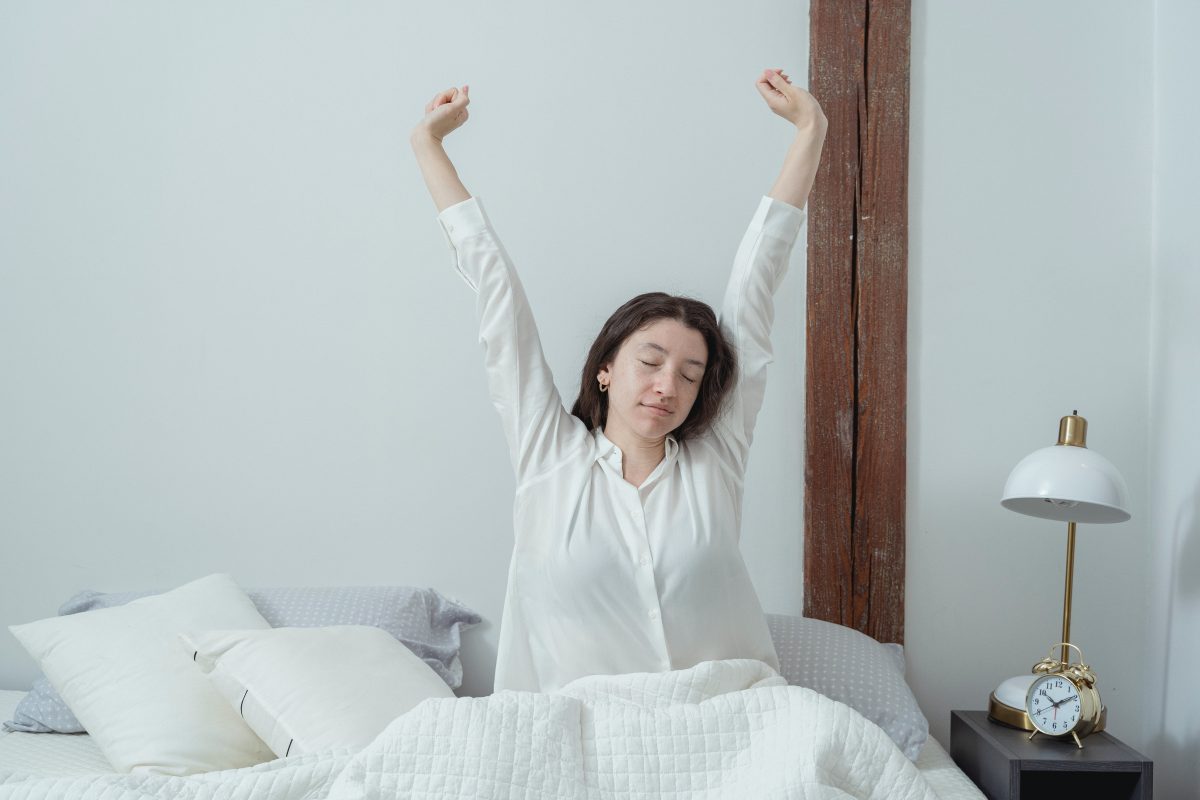 A sleepy woman stretching and waking up in bed in the morning.