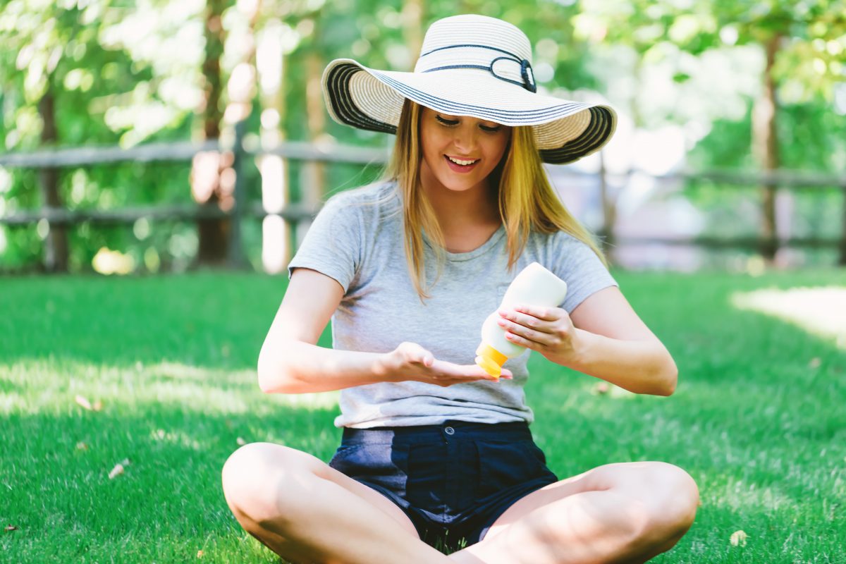 Young woman wearing a sun hat with a bottle of sunscreen outside on a summer day.