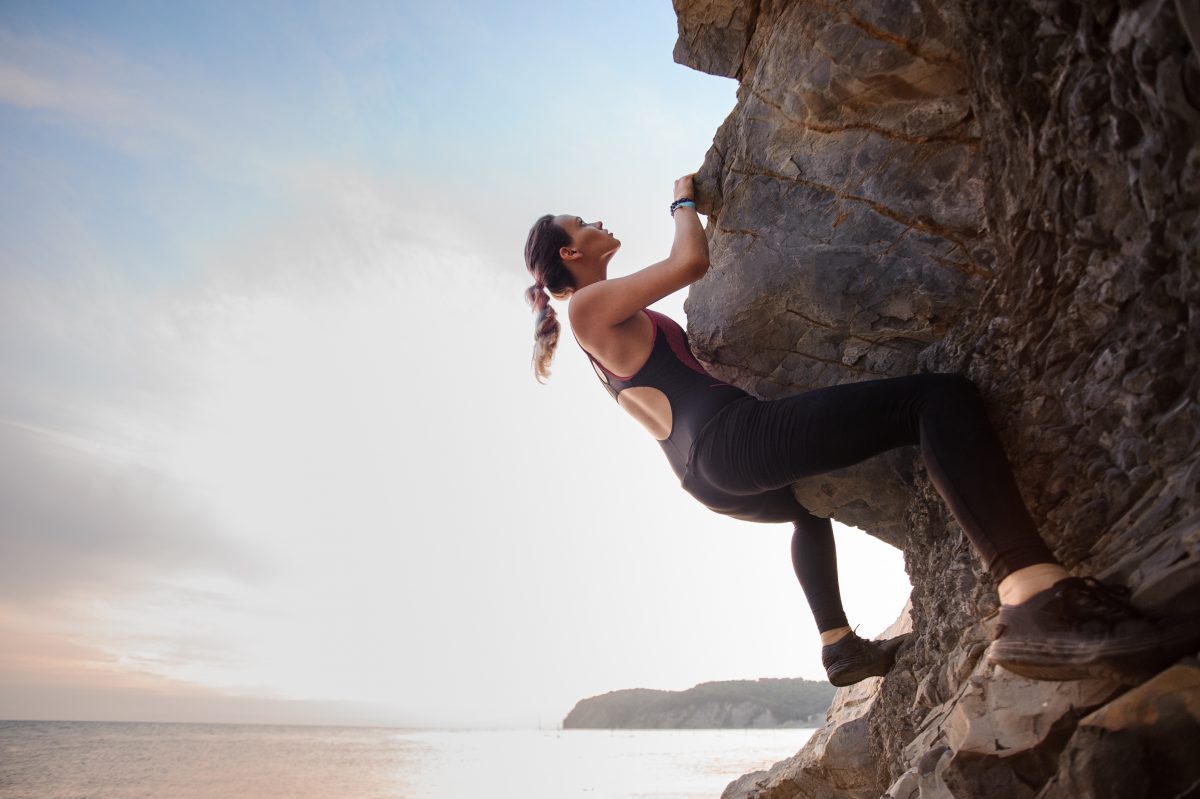Woman challenging herself to climb up an overhanging cliff.