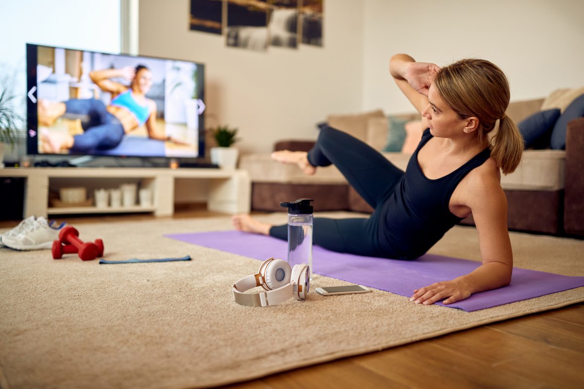 Woman in athleisure following a workout video on a flatscreen television screen, part of her glow up routine.