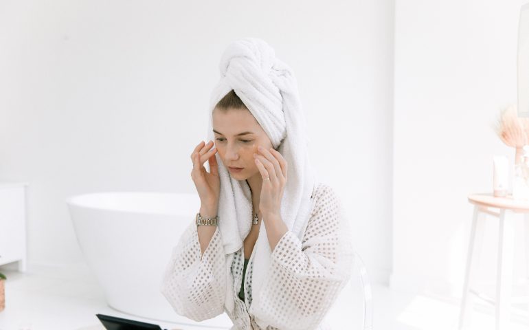 Woman wearing a bathrobe fresh out of the shower, applying under-eye patches.