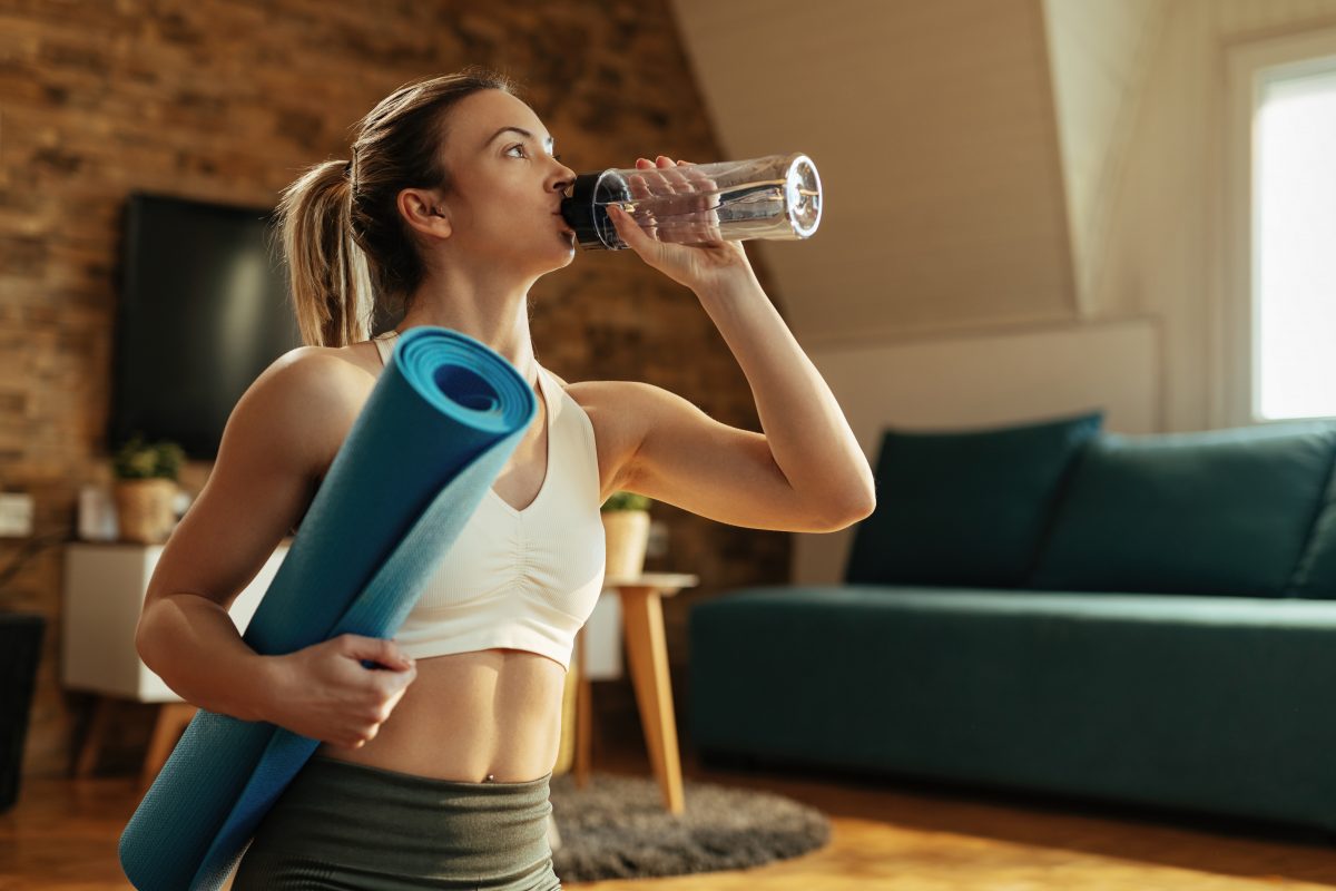 Woman in athleisure clothing drinking water after a home workout, one of the many ways on how to glow up.