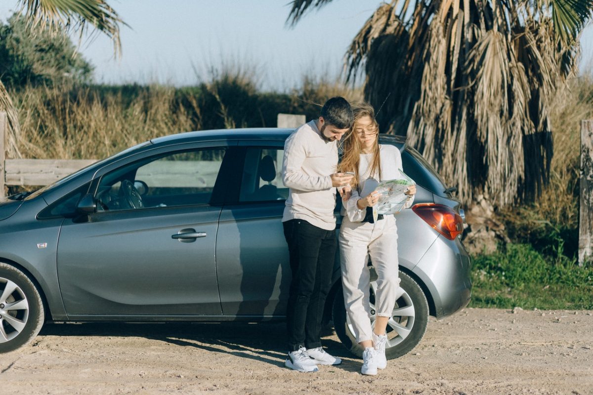 Man and woman standing beside a car while checking a map.