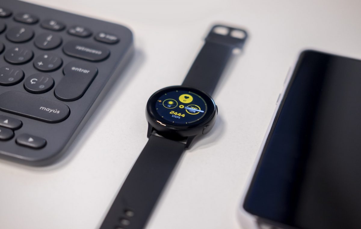 A black Samsung Galaxy Watch beside a keyboard and a cellphone