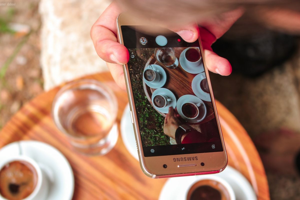 Hand holding a smartphone and taking photos of coffee.