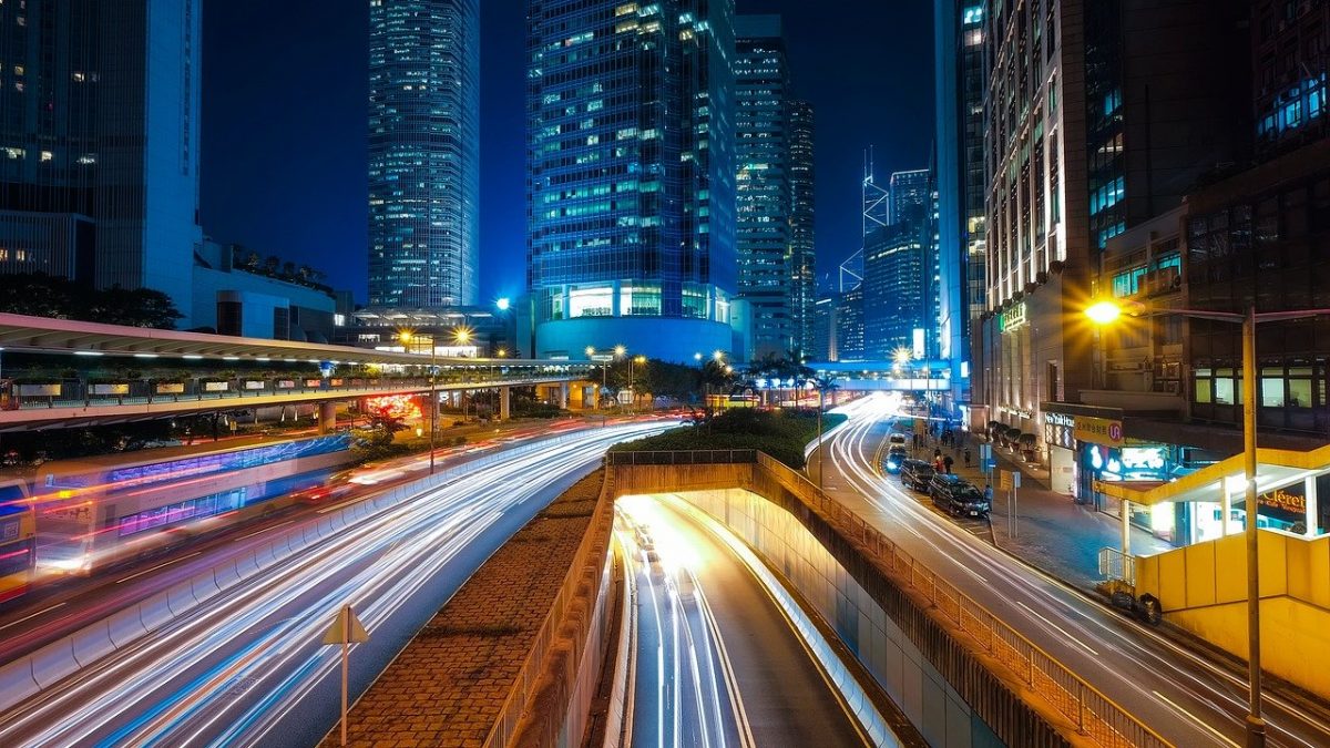 A long exposure photo of cars on the road with high rise buildings in the background.